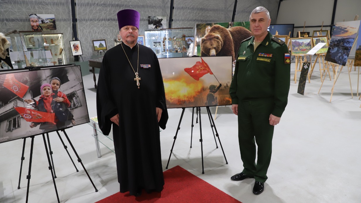 Протоиерей Александр Солдатенков (слева) и генерал-майор Олег Владимирский рядом с экспонатами фотовыставки, посвященной битве за Авдеевку Донецкой Народной Республики, которая завершилась 17 февраля 2024 года