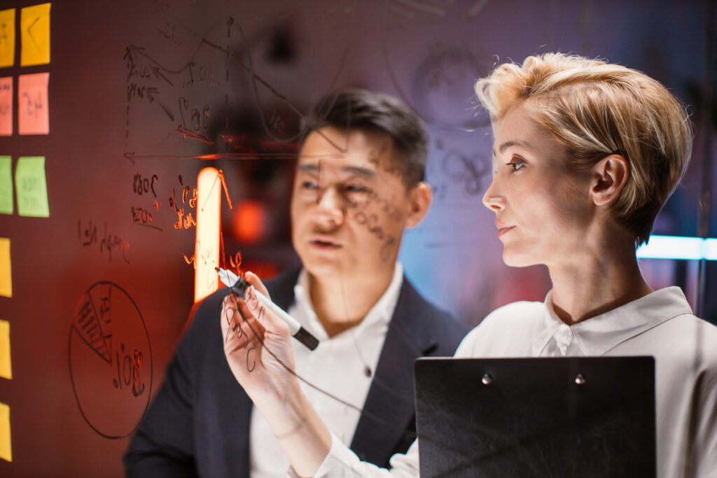 Двое коллег пишут маркером на стекле
