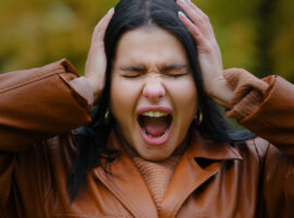 Как избавиться от стресса во время перемен? Portrait annoyed young hispanic woman outdoors screaming loudly in rage madly opening mouth holding hands on head headache feels frustrated pain horror hopelessness fear of violence expresses anger