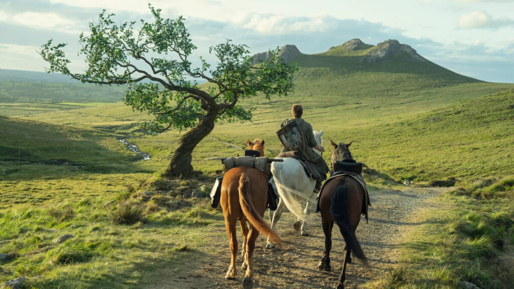 Кадр из сериала «Рыцарь семи королевств»: всадник едет по зелёным холмам с двумя лошадьми