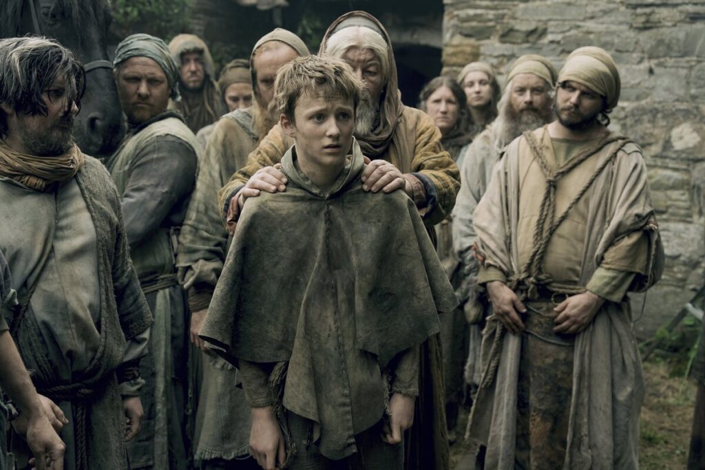Кадр из 2-й серии «Рыцаря семи королевств»: молодой парень стоит в толпе простолюдинов, старик держит его за плечи