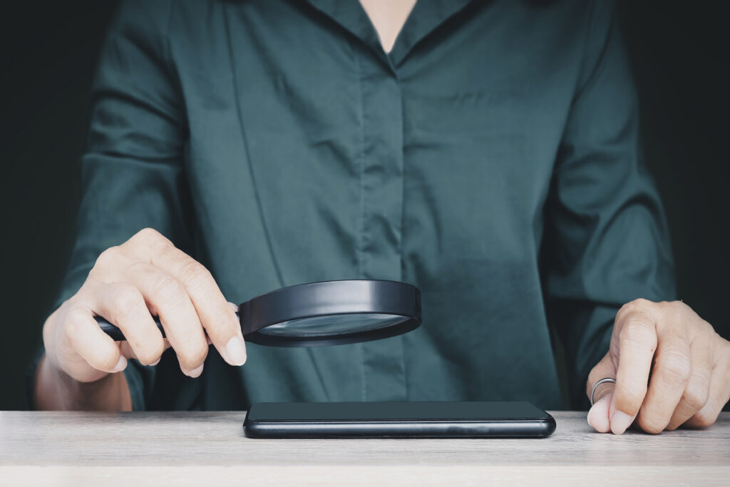 Человек, держащий увеличительное стекло над мобильным телефоном на столе