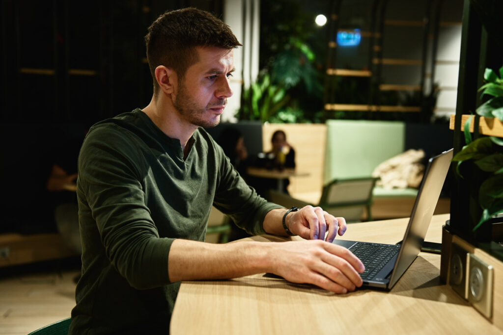 Мужчина печатает на клавиатуре ноутбука в кафе