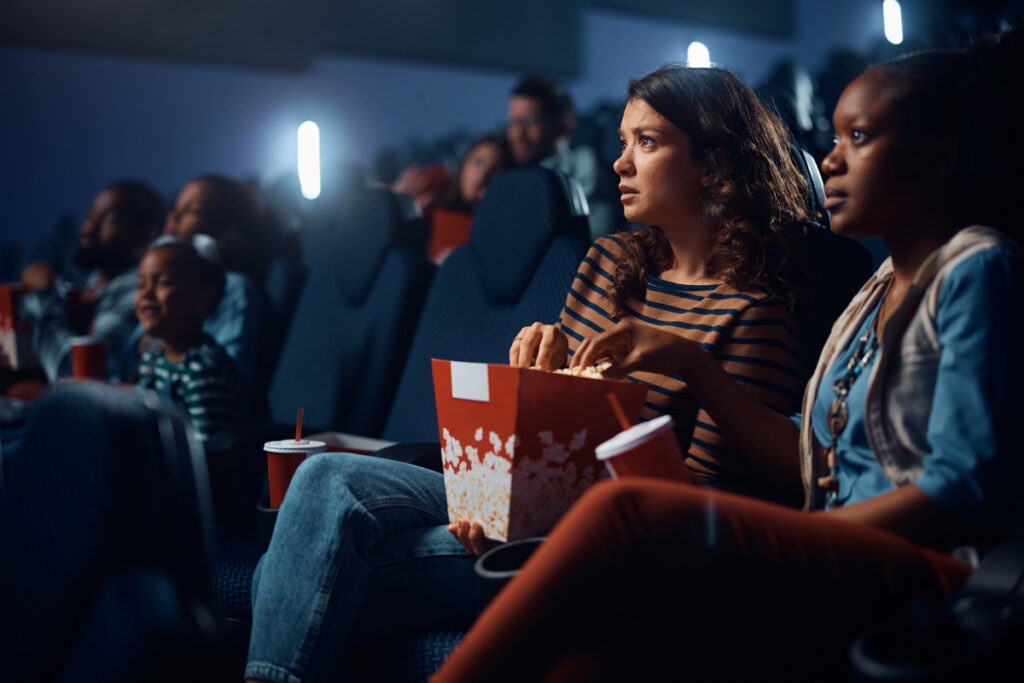 Молодые женщины едят попкорн во время просмотра фильма в кино