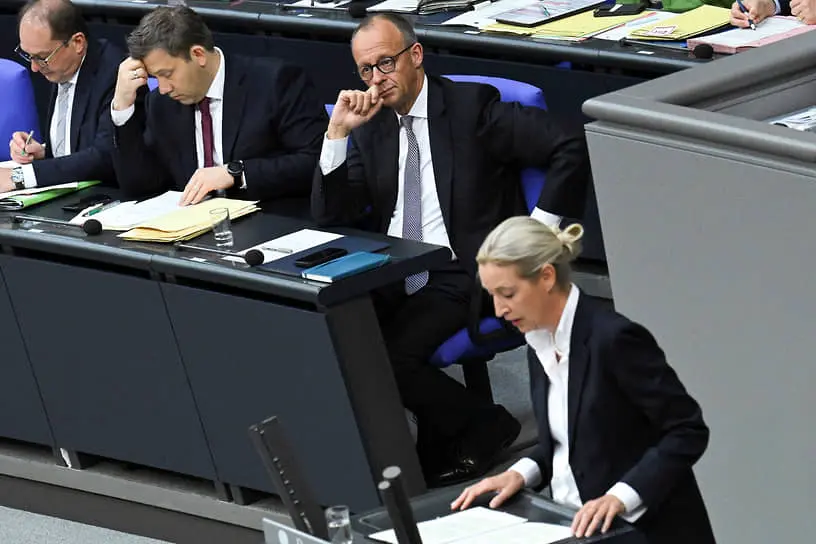 Канцлер Германии Фридрих Мерц (на заднем плане) смотрит за выступлением лидера «Альтернативы для Германии» Алис Вайдель в Бундестаге