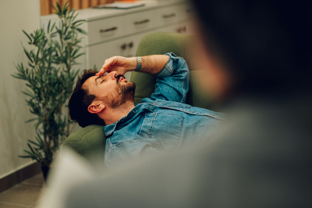 A depressed and anxious patient is lying down on a sofa in a psychotherapists office and discussing problems in life during the session - infovzor