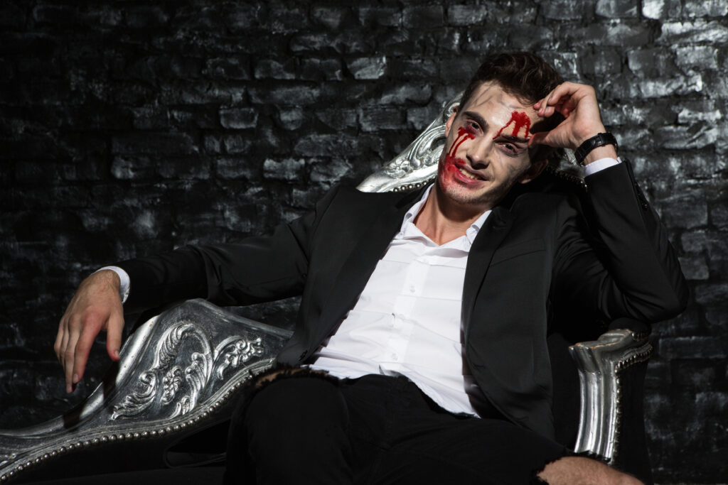 Smiling handsome vampire chilling on silver couch - infovzor Улыбающийся мужчина с кровью на лице сидит на диване