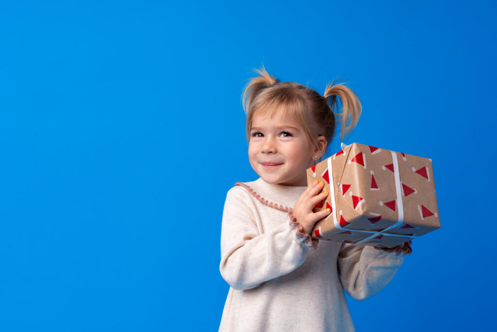 Happy little girl holding agift box on a blue background - infovzor Счастливая маленькая девочка держит подарочную коробку на прздник