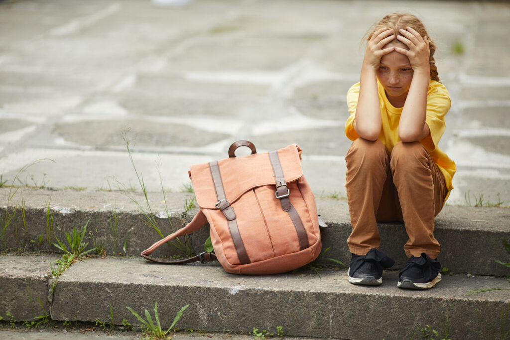 Грустная маленькая школьница сидит на лестнице на улице