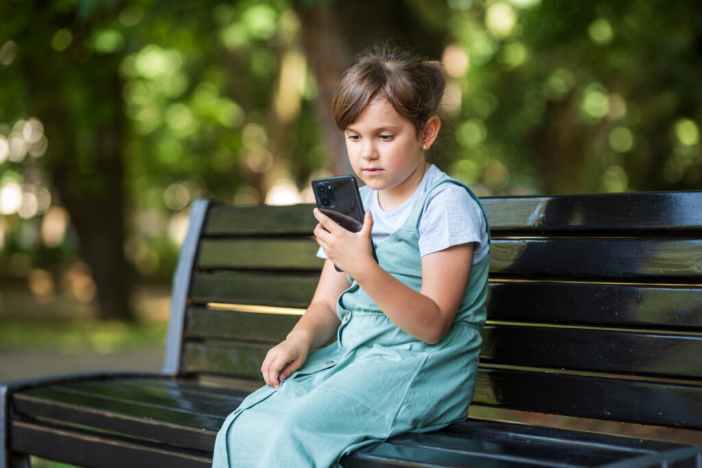 Девочка, использующая смартфон, сидит на скамейке в парке