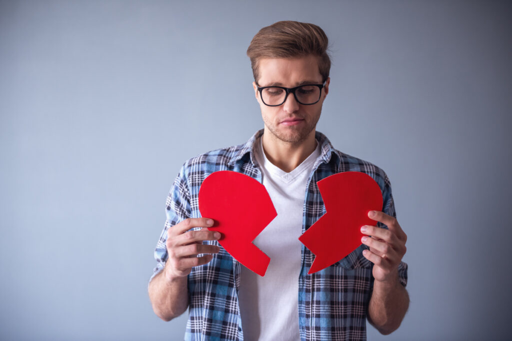Парень держит разрезанное картонное сердце в руках