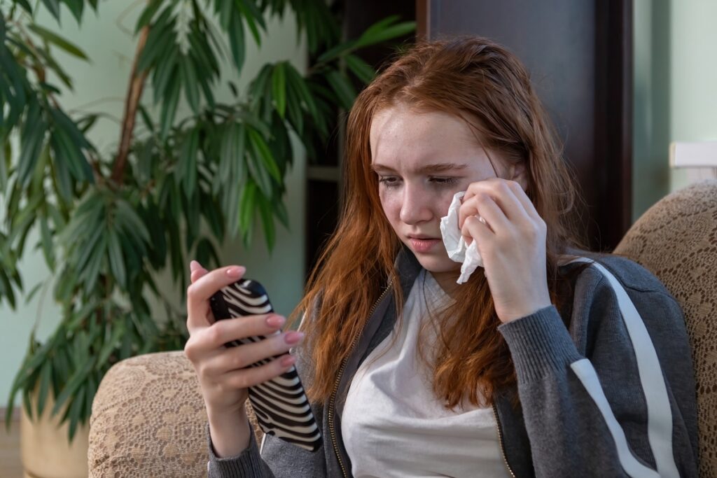 Плачущая девушка смотрит в смартфон