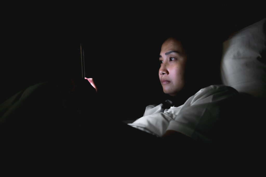 Женщина играет на смартфоне в постели по ночам