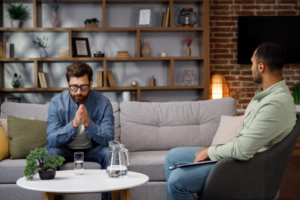 Visit to a psychologist A man sits on a couch and talks to a psychotherapist The patient is depressed apathetic and stressed from problems in his personal life Help of a psychologist - stanural мужчина на приеме у психолога