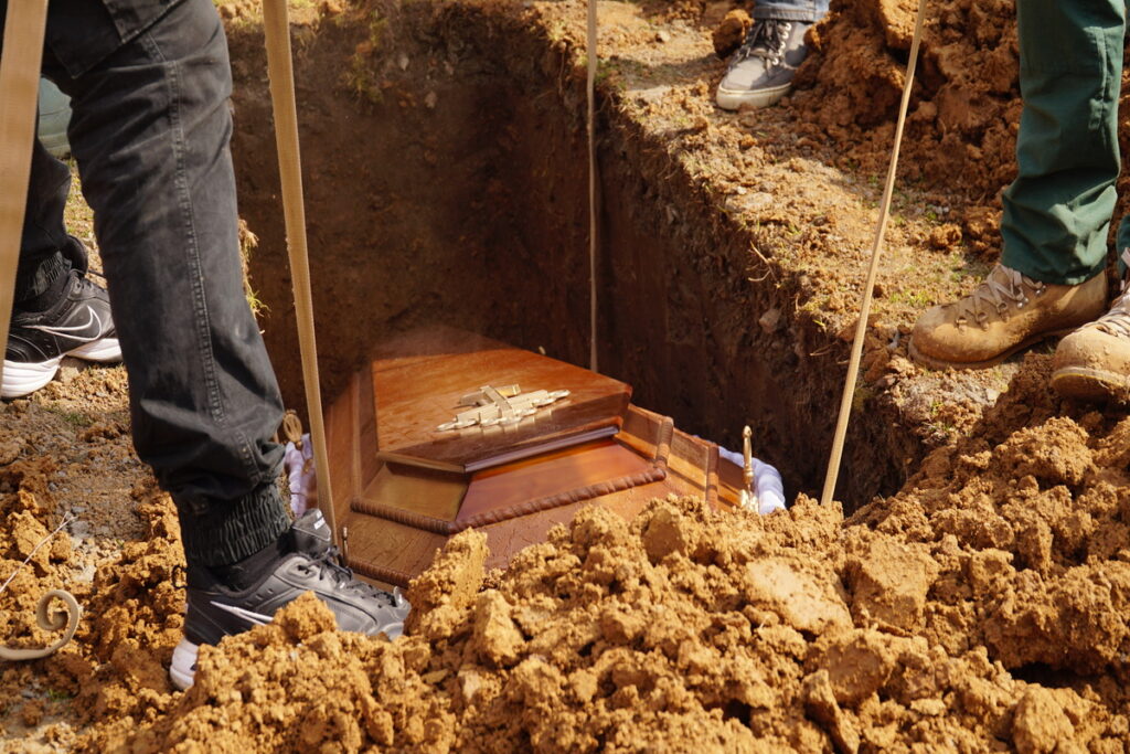 Мужчины опускают гроб в могилу