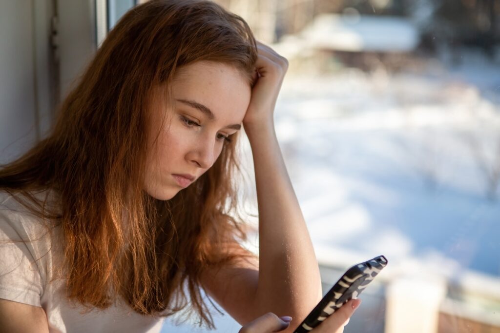 Девочка-подросток сидит на подоконнике и сидит в телефоне