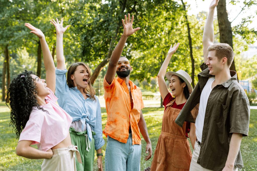 Группа из пяти молодых людей поднимает руки в парке