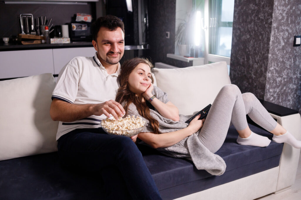 Молодая пара ест попкорн на диване, смотря фильм