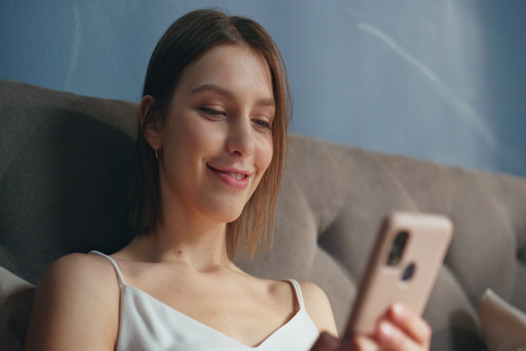 Женщина отдыхает на удобном диване и смотрит в телефон