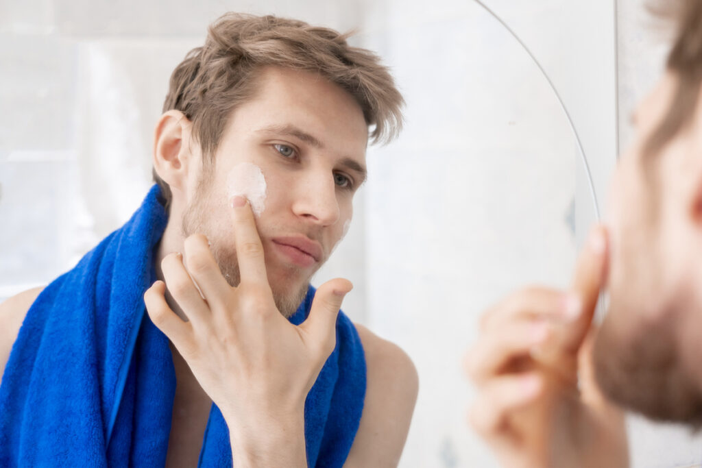 Молодой человек наносит крем на лицо