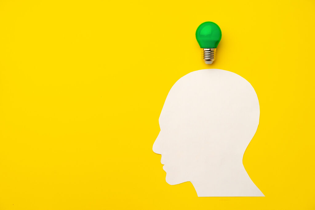 Вырезанная из бумаги голова и лампочка на бумажном фоне