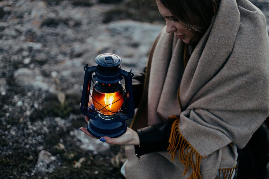 девушка в теплом пледе держит в руках керосиновую лампу