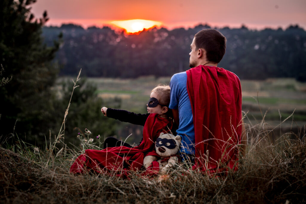 Мужчина в костюме супермена сидит на траве с ребенком