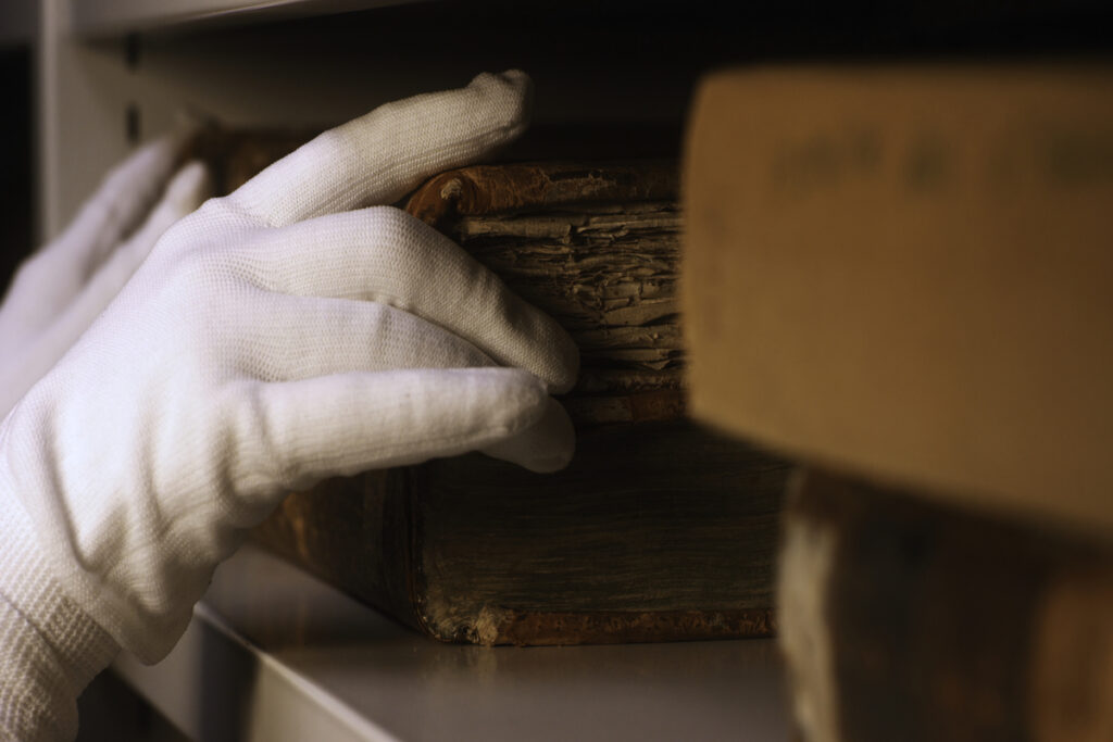 Рука в белой хлопчатобумажной перчатке, берущая очень старую книгу