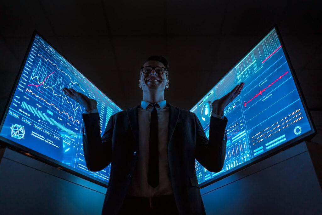 Улыбающийся бизнесмен стоит между синими экранами в темной лаборатории