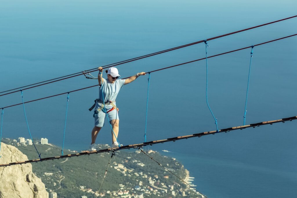 Молодая девушка идёт по верёвочной лестнице между скалистыми выступами
