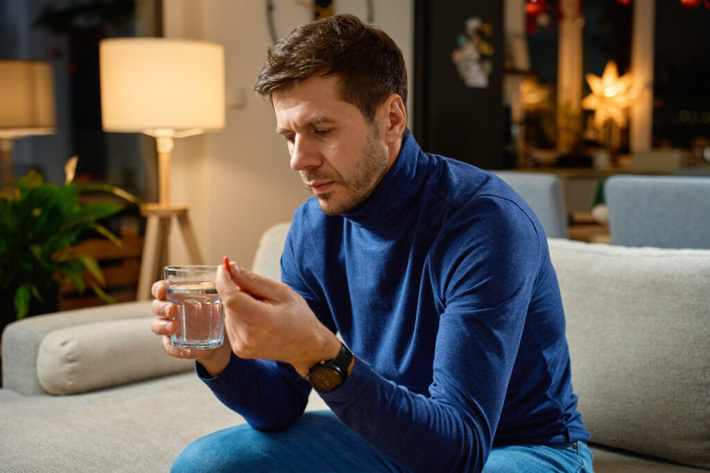 Мужчина сидит на диване с таблеткой и водой