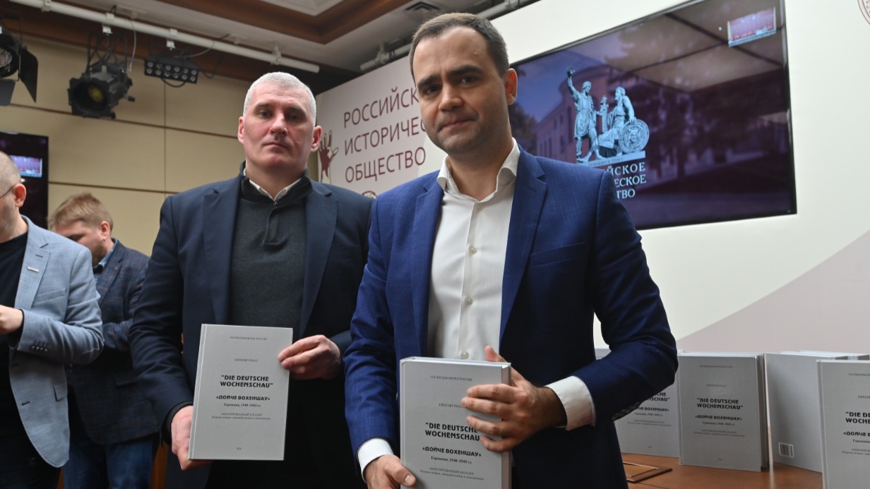 Начальник отдела анализа отечественного и зарубежного фонда аналитического департамента Госфильмофонда РФ Денис Федорин (слева) и гендиректор Государственного фонда кинофильмов РФ Денис Аксенов показывают аннотированный каталог киножурнала Die Deutsche Wochenschau («Немецкая кинохроника»)