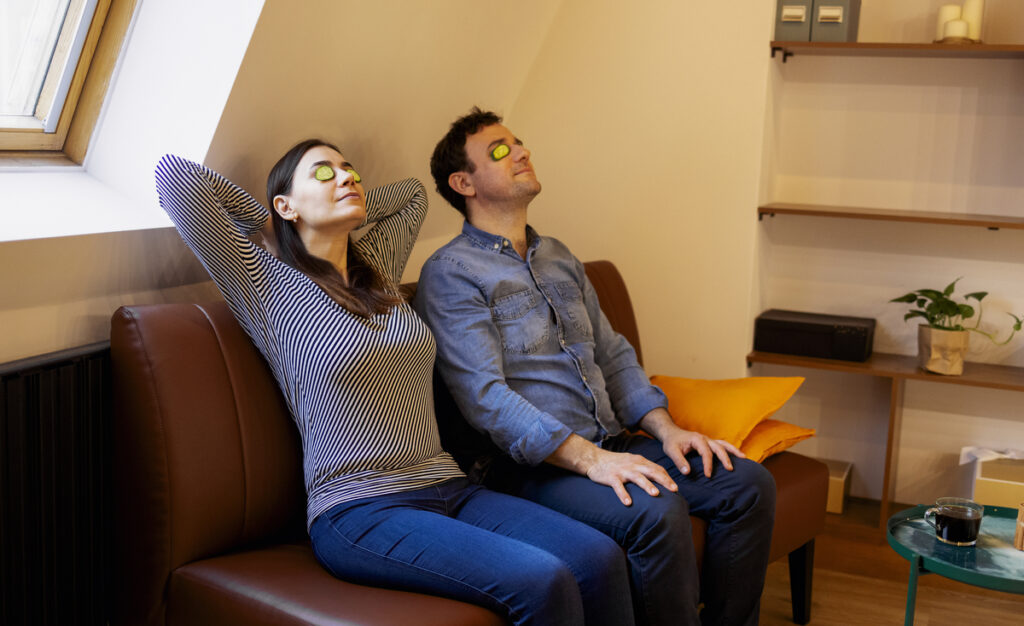 мужчина и женщина с огурцами на глазах расслабляются на диване