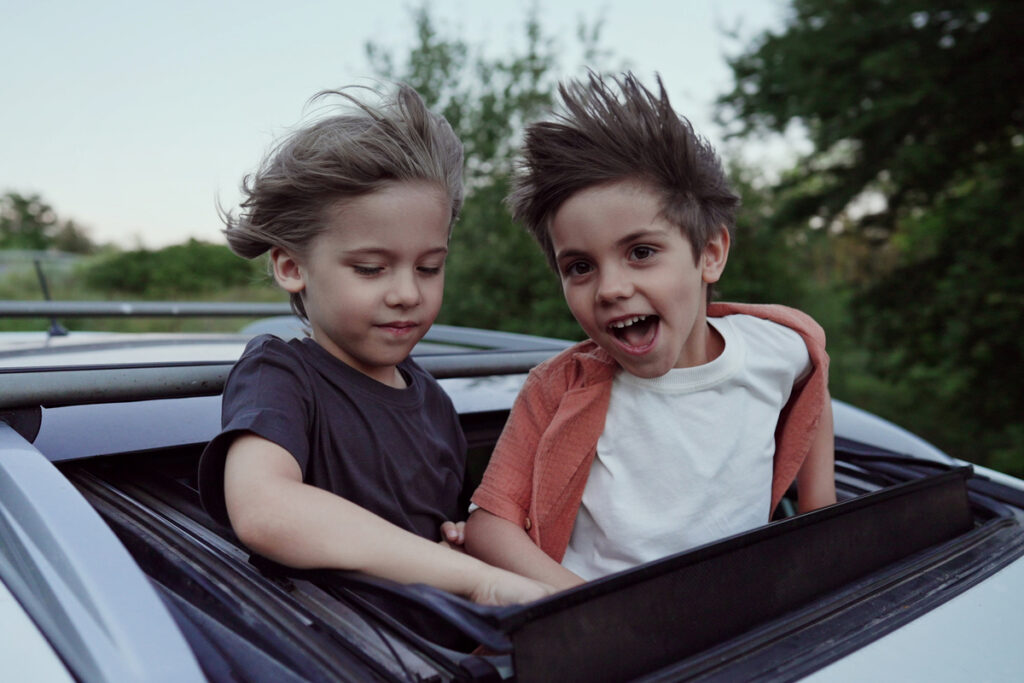 Забавные счастливые маленькие мальчики стоят в открытом люке автомобиля