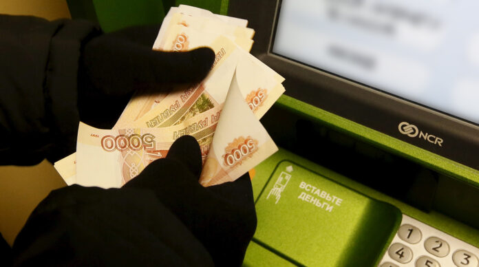 Man counts Russian rouble banknotes while he uses ATM bank machine at branch of Sberbank in Krasnoyarsk