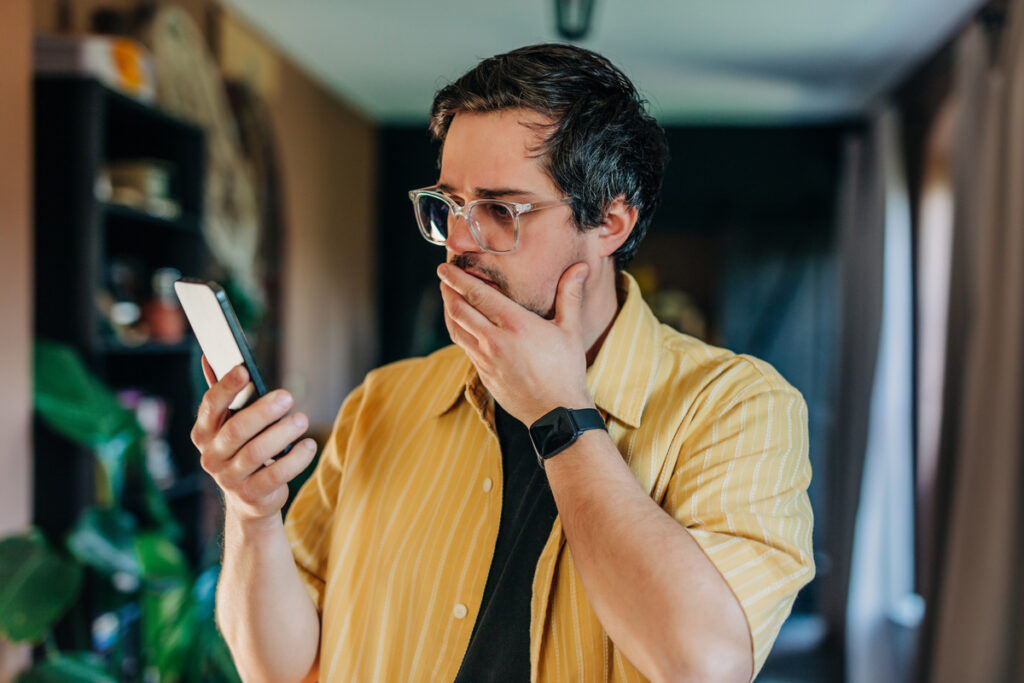 Мужчина в шоке смотрит на экран своего телефона