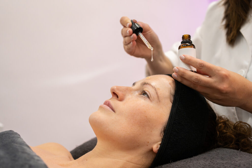 Косметолог наносит сыворотку на лицо клиента