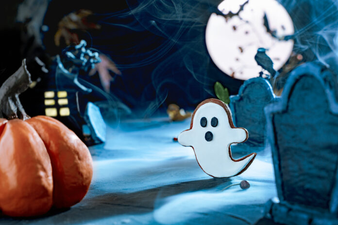 Scary Halloween background. Night scary cemetery with gravestones under the blue light of the moon. Flying cute spooky ghost. Bat silhouettes. Cemetery in the fog. copy space. Летающий призрак
