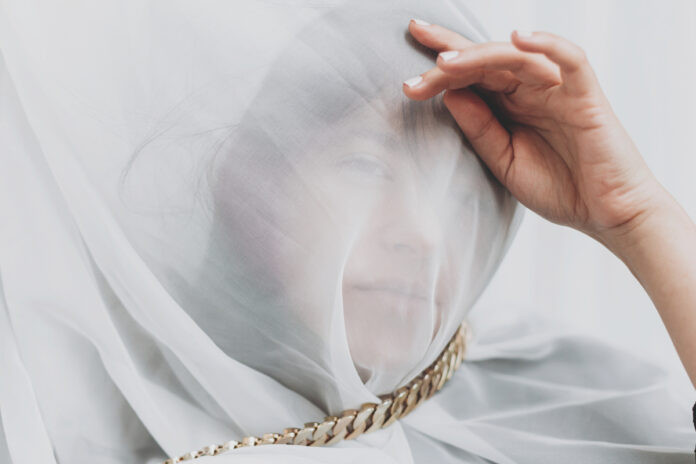 Beautiful woman under veil posing with golden necklace in room. Красивая женщина под вуалью