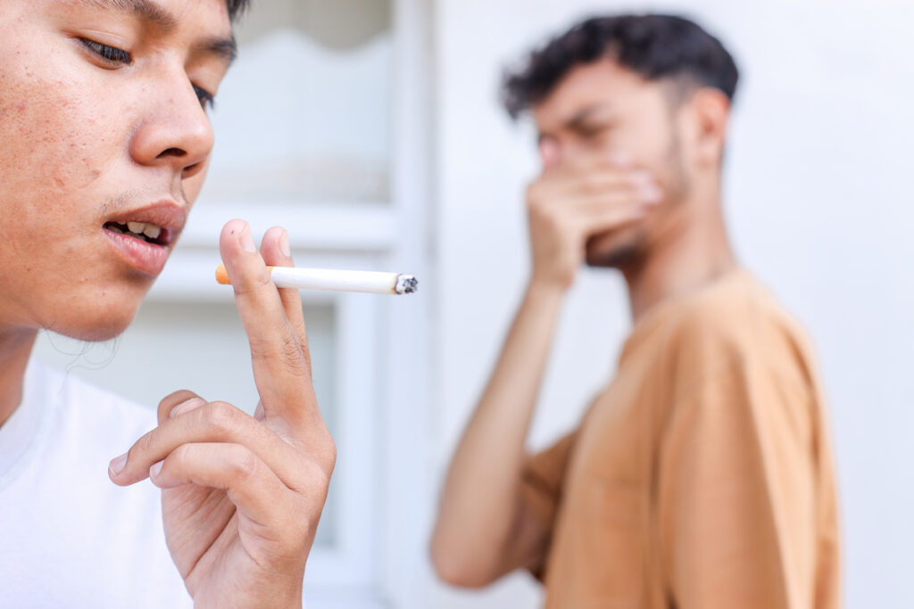 Мужчина курит сигарету, а другой закрывает нос