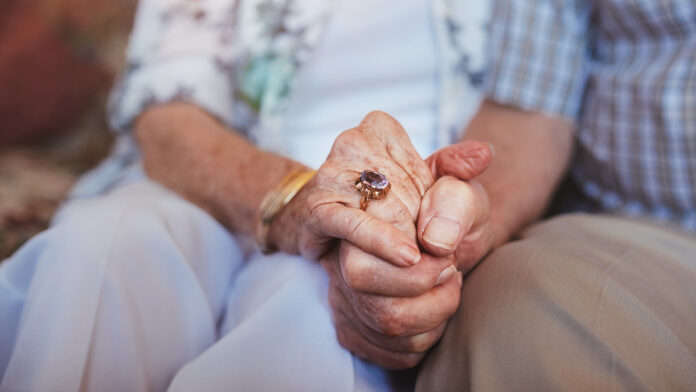 CroppedShotOfElderlyCoupleHoldingHandsWhileSittingTogether