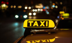 Yellow and black sign of Taxi placed on top of a car at night