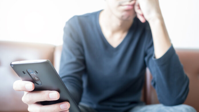 AnAsianYoungManLookingAtASmartPhoneIn