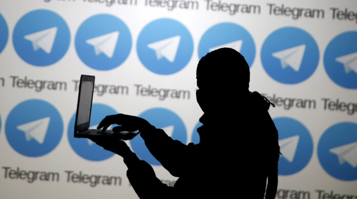 A man poses with a laptop in front of the Telegram logos in this picture illustration taken in Zenica