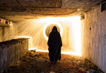 Человек в черном плаще перед светящимся кругом