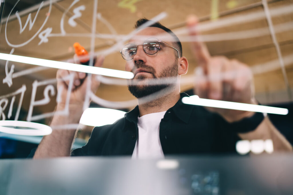 Серьезный мужчина рисует диаграмму на стеклянной стене