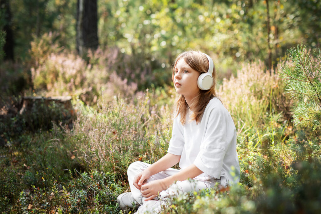 Девочка-подросток слушает музыку в наушниках в лесу
