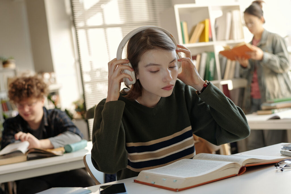 Девушка в наушниках занимается в школьной библиотеке