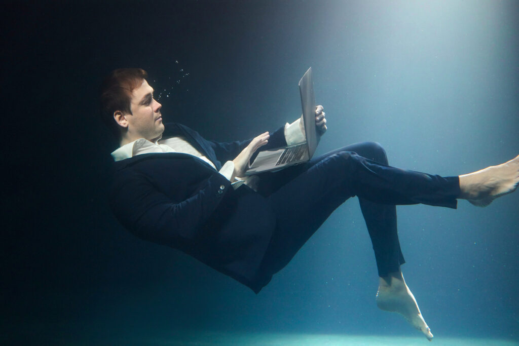 Мужчина использует ноутбук под водой в деловом костюме