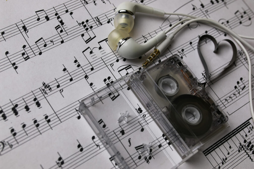 На этом студийном снимке на нотном листе лежат кассета и белые наушники